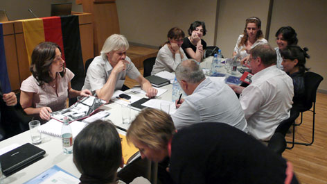 Many people sitting around a table covered with documents (Opens a Larger Version of the Image)