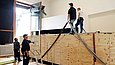 Zwei Männer stehen auf einer mit Gurten umspannten Kiste, zwei weitere sehen von unten zu