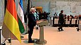 Ein Mann spricht an einem Pult, hinter ihm Länderflaggen (Deutschland und Usbekistan)