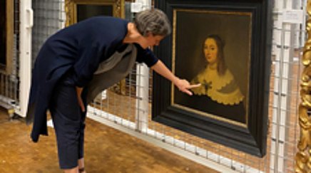 A woman looks at a painting in the storage room