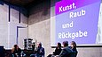 Fünf Menschen sitzen auf Stühlen auf einer Bühne