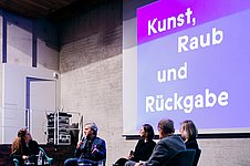 Fünf Menschen sitzen auf Stühlen auf einer Bühne