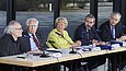 Fünf Personen sitzen an einem Tisch mit Mikrofonen