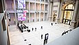 Menschen laufen durch eine hohe Halle mit Galerien.