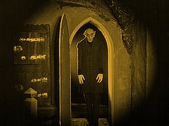 Dunkle Filmszene aus „Nosferatu“ mit einer Gestalt in einem Torbogen.