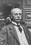 A historical black-and-white portrait of Eduard Arnhold. The man with a moustache is sitting in a suit in front of an interior backdrop and looking into the camera.