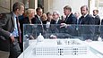 Mehrere Menschen sehen sich ein plastisches, weißes Gebäude-Modell unter einem Glas-Schaukasten an