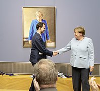 Angela Merkel and Jérémie Queyras shake hands in front of the portrait.