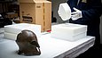 Tisch mit einem Metallhelm, einem Pappkarton und verschiedenen Schaumstoffteilen in unterschiedlichen Größen