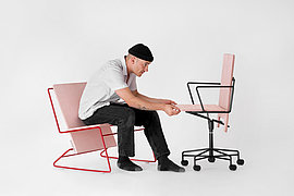 Ein Mann sitzt auf einem tiefen Stuhl und betrachtet vor sich einen Schreibtischstuhl