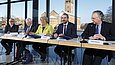 Fünf Personen sitzen an einem Tisch mit Mikrofonen