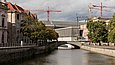 Blick über einen Fluss auf eine Stadt vor wolkenverhangenem Himmel