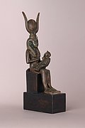 Sitzende Bronzestatuette der Göttin Isis mit dem Horus-Knaben auf dem Schoß und einer Sonnenscheibe zwischen Kuhhörnern auf dem Kopf.