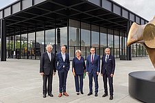 Fünf Personen posieren vor einem modernen Gebäude aus Glas und Stahl