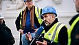 Mann mit Bauhelm und Warnweste spricht in ein Mikrofon
