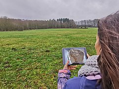 Frau hält Tablet vor Landschaft