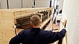 Ein Mann blickt auf eine an einer Seite offene Holzkiste, in der sich ein hölzernes Boot befindet