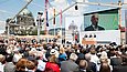 Drei Männer sprechen unter freiem Himmel auf einer Bühne vor Publikum