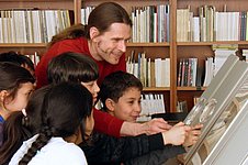 A man shows illustrations in a book to several children