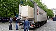 Drei Männer beobachten, wie eine große Holzkiste von einem Kran auf den Anhänger eines LKW verladen wird