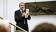 Ein Mann im Anzug steht auf einer Treppe und spricht in ein Mikrofon