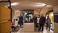 Blick in einen Museumsraum, in dem sich mehrere Menschen eine gläserne Vitrine ansehen