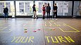 Menschen schauen sich eine Wandzeitung an, am Boden klebt buntes Klebeband 