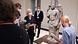 Frau präsentiert Gruppe eine steinerne, überlebensgroße hinduistische Statue
