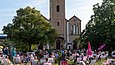 Menschen sitzen auf einer Wiese vor einer Kirche in der Sonne 