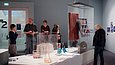 Mehrere Menschen sehen sich in einem Ausstellungsraum eine große Glasvitrine an