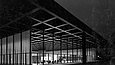 Schwarz-Weiß Fotografie mit Blick auf ein von innen beleuchtetes, modernes gläsernes Gebäude bei Nacht