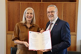 Marion Ackermann (links) und Jörg Dittrich halten gemeinsam die aufgeklappte Vereinbarung in die Kamera.