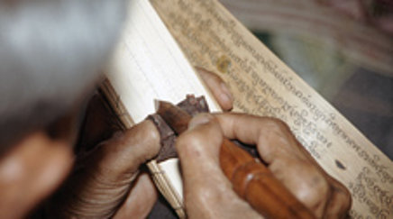 Ein Mann ritzt mit einem Griffel Text in ein Palmblatt