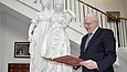 Ein Mann steht neben der Skulptur zweier Frauen in einem Treppenhaus und liest in einem Buch