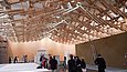 Besucher*innen in einem großen Saal mit gigantischer ineinander verschachtelter Holzkonstruktion