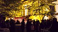 Mehrere Menschen stehen am Abend vor einem beleuchteten Gebäude