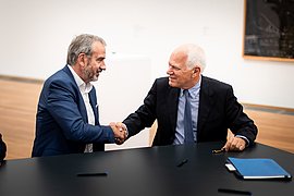 Hermann Parzinger und Axel Marx schütteln sich die Hände an einem Tisch