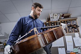 Barnes Ziegler hält ein Violoncello mit weißen Handschuhen und betrachtet das Instrument.