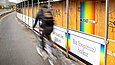 Bauzaun mit Plakaten, daneben fährt ein Radfahrer vorbei