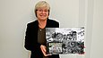 Eine Frau hält eine schwarz-weiß Fotografie hoch und lächelt