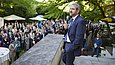 Mann im Anzug mit Mikro in der Hand steht an einer steinernen Balustrade und hält Rede vor Festgemeinschaft