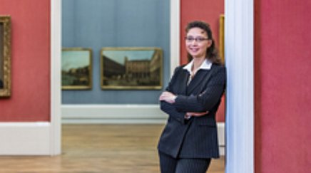 A woman stands in a museum with paintings