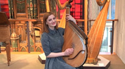 A seated woman holds a large stringed instrument in her hand