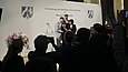 Zwei Männer und eine Frau beglückwünschen eine ältere Dame auf einer Bühne