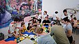 Menschen diversen Alters sitzen an einem großen Tisch und basteln