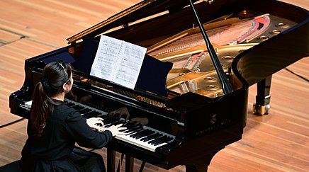 Frau sitzt an einem Flügel und spielt Klavier