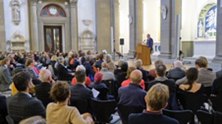 Ein Mann an einem Pult in einer Kirche spricht zu einem Publikum