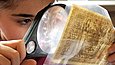 A child examines a bank note through a magnifying glass