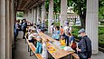 Menschen basteln an Biertischen in einem Säulengang