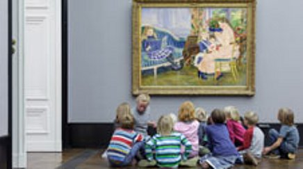 A woman and a group of children sit on the floor in front of a painting